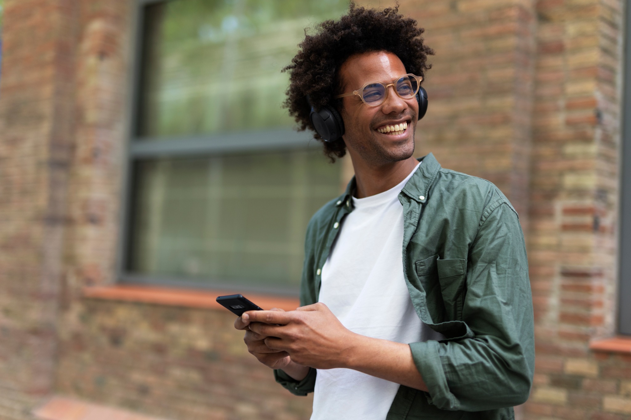 A man with headphones smiling while holding his phone